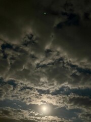 Obraz premium A bright full moon in a cloudy night sky. This phenomenon highlights the reflected sunlight from the moon against the dark sky, while the cloud cover softens it.