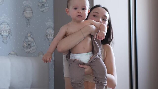 Mother changing babies clothes in bedroom.