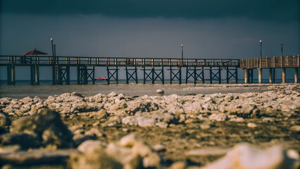 An empty wooden pier over bleached coral and deserted beach structures shows how warming seas and reef loss devastate coastal tourism and local economies.
