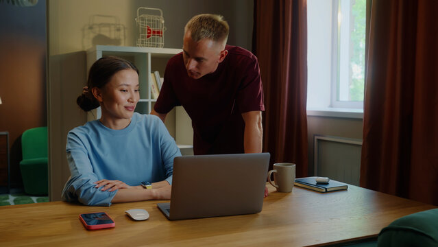 Boss man checks asian woman subordinate do task correctly report. Management satisfied work. Employee right answer. Good job. Guy show laptop screen. Multi racial national couple online shopping home.