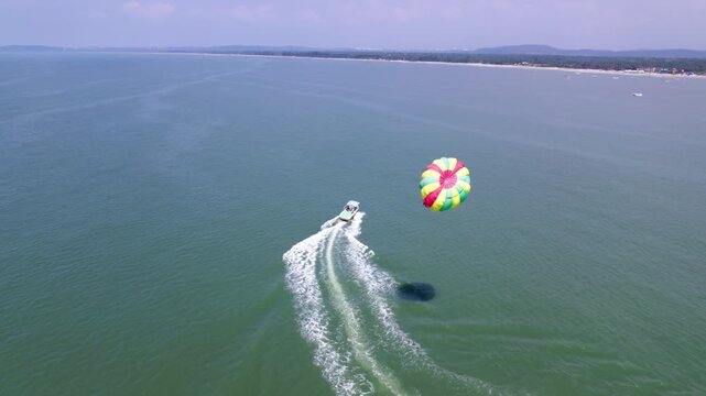 Speed boat parasailing with Arabian Sea, haze and greenery at colva, goa, india. day time, slight pan shot, drone shot, 4k.
