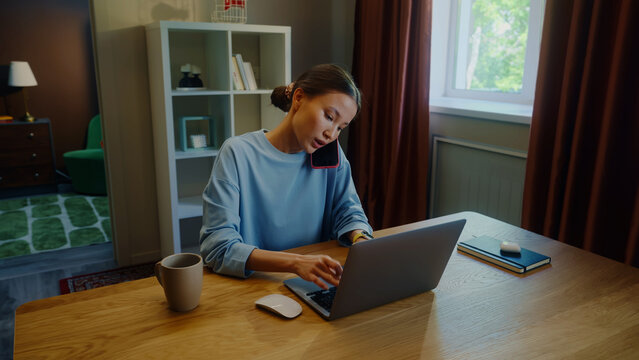 Asian woman worker remote hard work laptop home. Girl talk mobile cell phone. Female employee answer call. Busy ceo person use pc. Online education. Computer freelance. Distant consult center job.