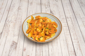 Patatas bravas served in a clay bowl, with a deep red, thick sauce, and a sprinkle of chopped parsley for garnish.