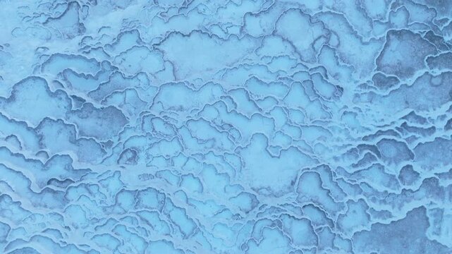 Aerial drone footage of the white travertine terraces of Pamukkale in Turkey, filled with natural thermal water pools. The bright mineral formations create a striking contrast with the surrounding lan