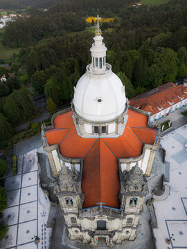 Aerial view of the Sameiro Sanctuary's dome and cross stand proudly against the sky, its terracotta roof glowing warmly amidst the cool, grey stone and lush greenery, Braga, Braga, Portugal.