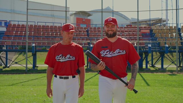 Close-up of the coach giving instructions to the baseball player with a bat.. Players walk with the coach across the field and discuss game techniques.