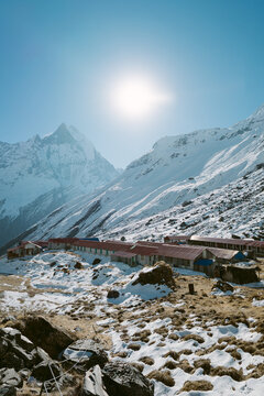 View of sun shining over snow-capped peaks towering above a row of buildings nestled in a valley, Himalaya, Annapurna, Nepal.