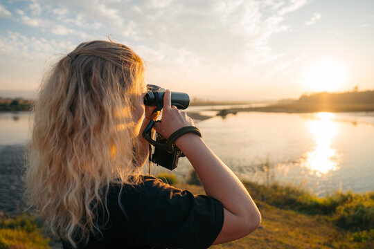 View of a blonde woman with a camera capturing the golden sunlight reflecting on the tranquil river, Himalaya, Annapurna, Nepal.