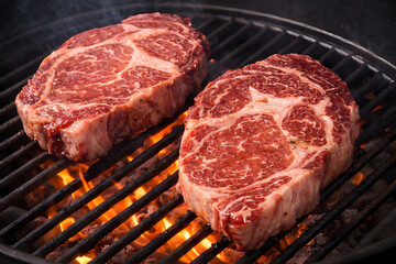 Two steaks are being grilled over an open flame on a barbecue