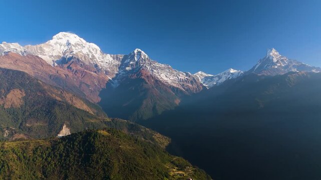 Aerial view of majestic Annapurna mountain range with snow-capped peaks and lush green valleys bathed in sunlight, Himalaya, Annapurna, Nepal.