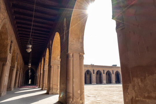 Ibn Tulun Mosque in Cairo features arched corridors with sunlight streaming through. The architecture showcases Islamic design elements and historical significance.