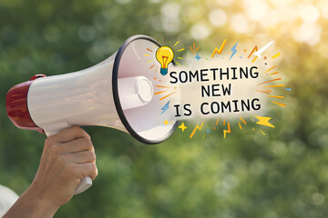 A hand holding a megaphone with a lightbulb and text announcing something new is coming