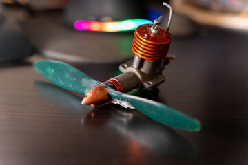 Small model engine with a propeller placed on a dark surface in a workshop setting