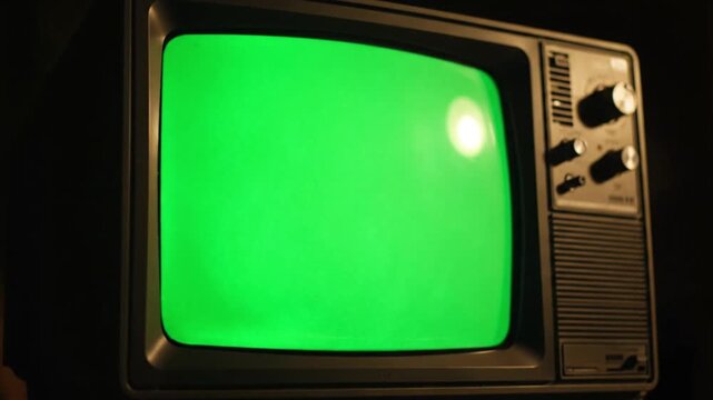 Close-up of an old television with a bright green screen, tv green screen, against a dark background.
