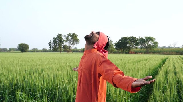 happy indian farmer standing at green wheat field