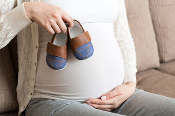 Small shoes for the unborn baby in the belly of pregnant woman ion sofa at the house