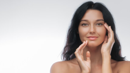 Fototapeta premium Beautiful Woman Touching Face in Studio with Clean Glowing Skin Look