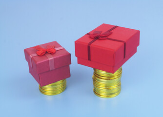 Fototapeta premium Red gift boxes on gold coins stacks. Different cost of gifts concept.