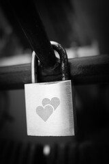Close-up photograph of a metal love padlock engraved with two hearts, attached to a railing.