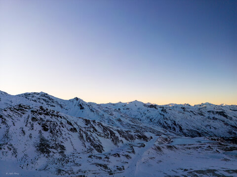 Aerial view of snow-capped peaks meet the soft gradient sky, where icy whites contrast with the warm hues of the horizon, Les Belleville, Auvergne-Rhone-Alpes, France.