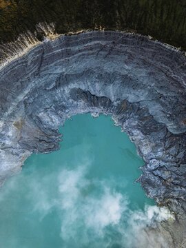 Aerial view of the breathtaking turquoise lake nestled within the rugged, layered caldera of Kawah Ijen, a volcanic marvel in East Java, Indonesia.