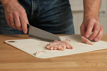 Man butcher cut raw meat with sharp knife at home kitchen. Male person cutting the chicken fillet pieces for cooking. Preparing chopping food. Split poultry breast. Healthy lean meat, low cholesterol