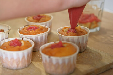 Person decorating cupcakes. Baker piping swirl of a creamy blue purple frosting onto a freshly baked cupcake. Decorated cakes with colorful sprinkles. Sweet Dessert Preparation. Pastry small business