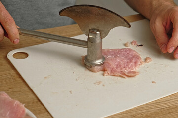 Person using meat tenderizer on raw chicken. Chef preparing pork loin slice with meat mallet on cutting board. Man tenderizing fillet. Cooking cutlets pounding poultry breast close-up. Culinary dish.