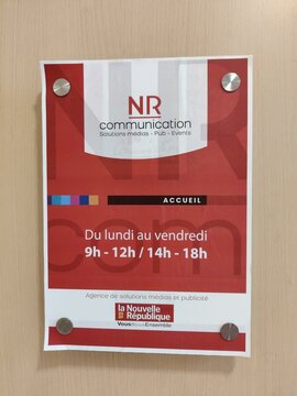 Poitiers, France - January 14, 2026: NR Communication office sign displaying operating hours and services, mounted on a wall with visible fasteners and a colorful design