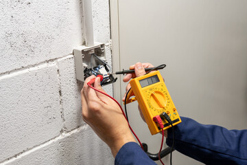 Close-up on an hands of electrician fixing an electrical outlet and measuring the voltage at a warehouse - improvement concepts