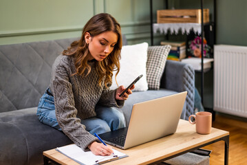 Pensive adult woman is using smartphone and laptop to calculate home finances.