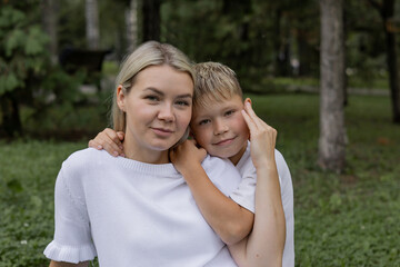Fototapeta premium Portrait of a mother and son in a park. A Caucasian young woman with a blond boy outdoors. 