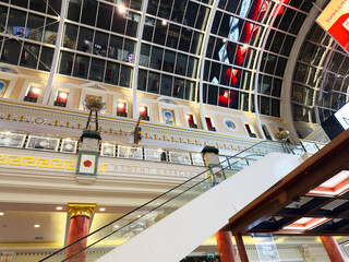 Naklejka premium Elegant glass atrium mall interior in Manchester with escalator, ornate decor, and bright skylight