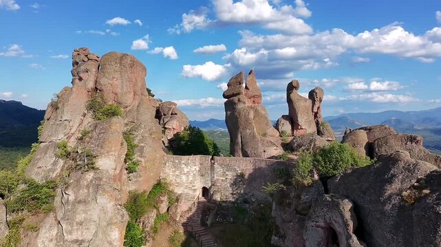 Aerial drone view of Belogradchik Fortress walls surrounded by ancient rock formations. Historic stone structures blend with dramatic landscape in northern Bulgaria