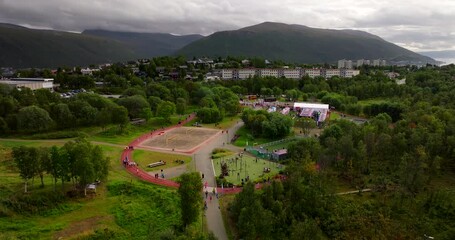 Aerial drone view of the Relay for Life charity run in Tromso. People walk and run on a track in a park, surrounded by green trees and mountains. Ideal for community and fundraising concepts
