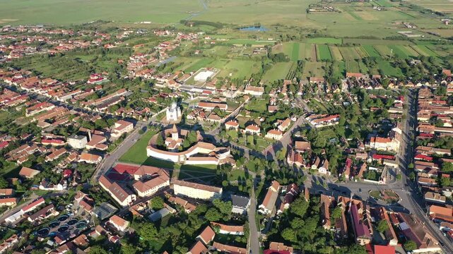 Aerial view of the fortified church, a blend of red-roofed buildings and lush greenery, with a backdrop of expansive fields, Prejmer, Brasov, Romania.