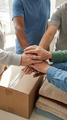 Group of people stacking hands above a cardboard box indoors  