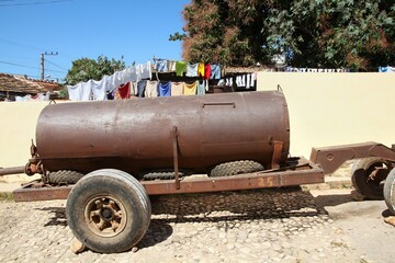 Poverty in Cuba. Water delivery trailer parked in Trinidad, Cuba. Home welded water tank on a trailer with worn bald tyres, wheel missing screws, and faulty brakes requiring stones under wheels.