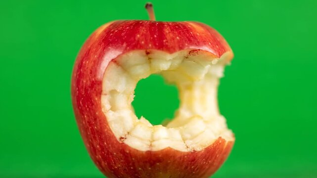 Close-up of a partially eaten red apple on a vibrant green background.