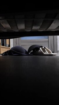 Vertical video. View from under wobbly bed where couple makes love. Someone undresses woman and throws her underwear on floor next to bed. Woman's bra falls onto slippers. Man and woman have sex.