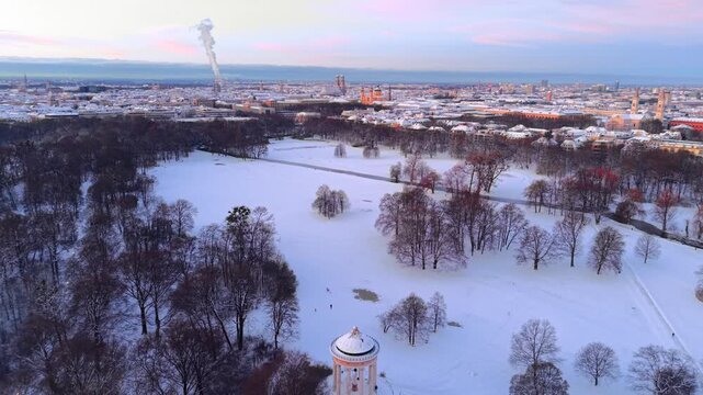 Cinematic dawn over historic Munich in winter. Breathtaking sunrise illuminates the snow-covered rooftops of the Altstadt and the Greek-style Monopteros temple in a frosty park landscape