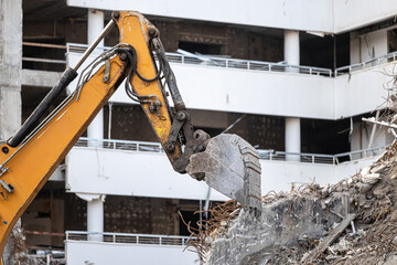 Demolition industry. A heavy-duty yellow hydraulic excavator with a large bucket working on a demolition site of a reinforced concrete building. Old building demolition process.