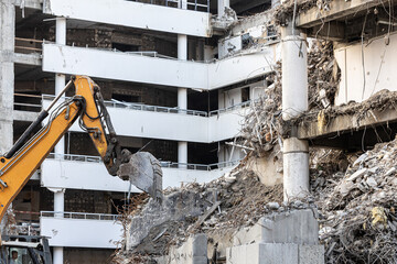 Demolition industry. A heavy-duty yellow hydraulic excavator with a large bucket working on a demolition site of a reinforced concrete building. Old building demolition process.
