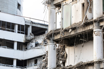 Demolition industry. A heavy-duty yellow hydraulic excavator with a large bucket working on a demolition site of a reinforced concrete building. Old building demolition process.