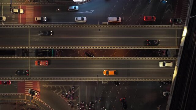 Top down aerial view of busy intersection in Bangkok, Thailand, at night, with cars, motorcycles, and skytrain moving through the city