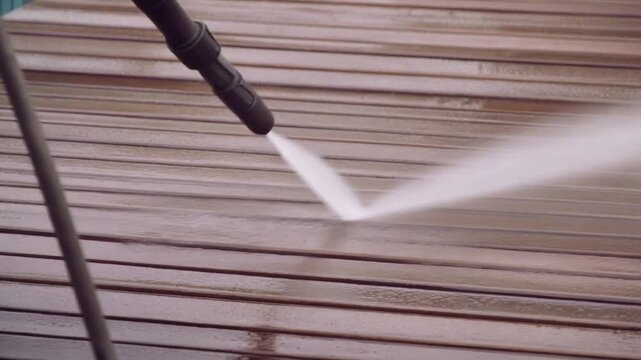 High pressure water jet cleans wooden deck surface. Spraying water on wet planks near pool. 
