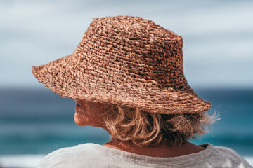 Handmade palm leaf sun hat worn by woman with blonde hair enjoying peaceful moment outdoors near ocean under bright sky