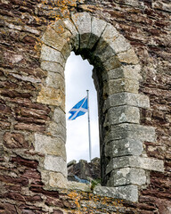 Naklejka premium Scottish flag flying at medieval Doune Castle seen through stone window in Scotland