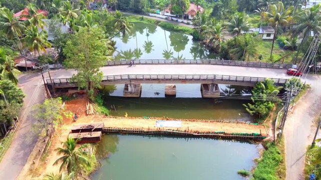 Aerial view of a rural river bridge in Kerala featuring lush greenery, coconut trees, traffic, and a temporary check dam construction.