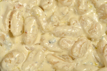 A close up top view shows a delicious portion of homemade gnocchi covered in a thick and smooth gorgonzola cheese sauce with visible spices